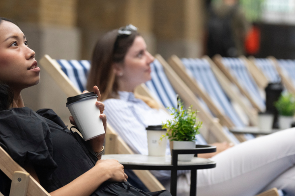 Two people sitting in deck chairs, one with a coffee cup in their hand. They are spectators at London Sports Festival.