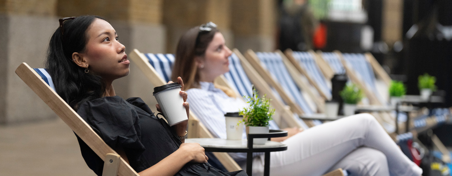 Two people sitting in deck chairs, one with a coffee cup in their hand. They are spectators at London Sports Festival.