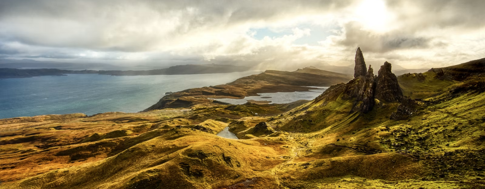 Rocky pinnacles of the Old Man of Storr rise above rolling green hills and a coastal loch on the Isle of Skye, a dramatic highlight among UK hiking routes