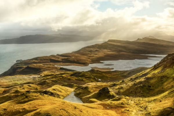 Rocky pinnacles of the Old Man of Storr rise above rolling green hills and a coastal loch on the Isle of Skye, a dramatic highlight among UK hiking routes