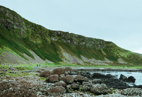 Basalt boulders line the shoreline of the Causeway Coast, with green headlands curving along the water's edge