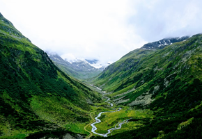 A river winds through the steep, cloud-covered slopes of Glencoe's Lost Valley in the Scottish Highlands