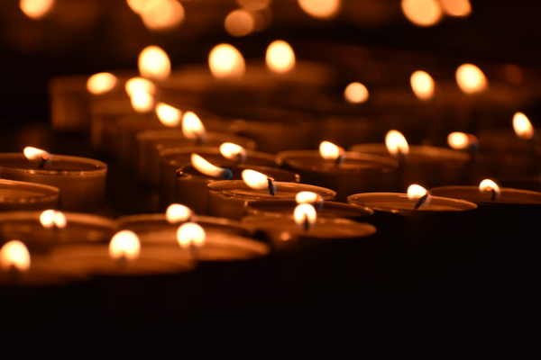Rows of small candles glowing in a dimly lit setting, creating a warm, atmospheric scene.