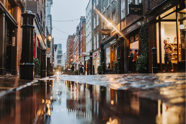 Rainy street in London with a large puddle on the street with warm lights reflecting in the puddle.
