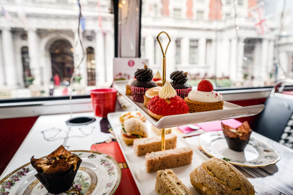 Afternoon tea with sandwiches, scones and assorted cakes served on a tiered stand beside a window overlooking a London street.