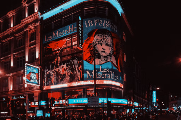 London theatre at night displaying illuminated Les Misérables posters and signs, with crowds gathered outside.