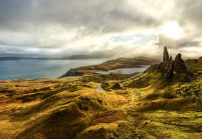 Rocky pinnacles of the Old Man of Storr rise above rolling green hills and a coastal loch on the Isle of Skye