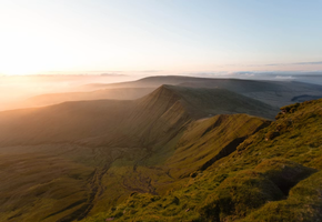 Sunrise light spreads across the ridgelines of Pen y Fan in the Brecon Beacons