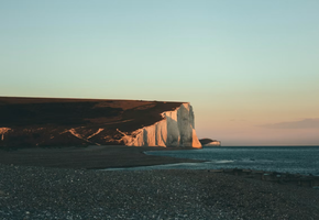 Chalk cliffs of the Seven Sisters meet the sea under a dusk sky on the South Downs coast.